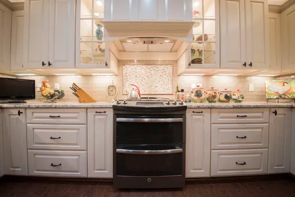 Cream-colored kitchen cabinets with a black stove centered in front of a colorful backsplash and dark wooden floor.