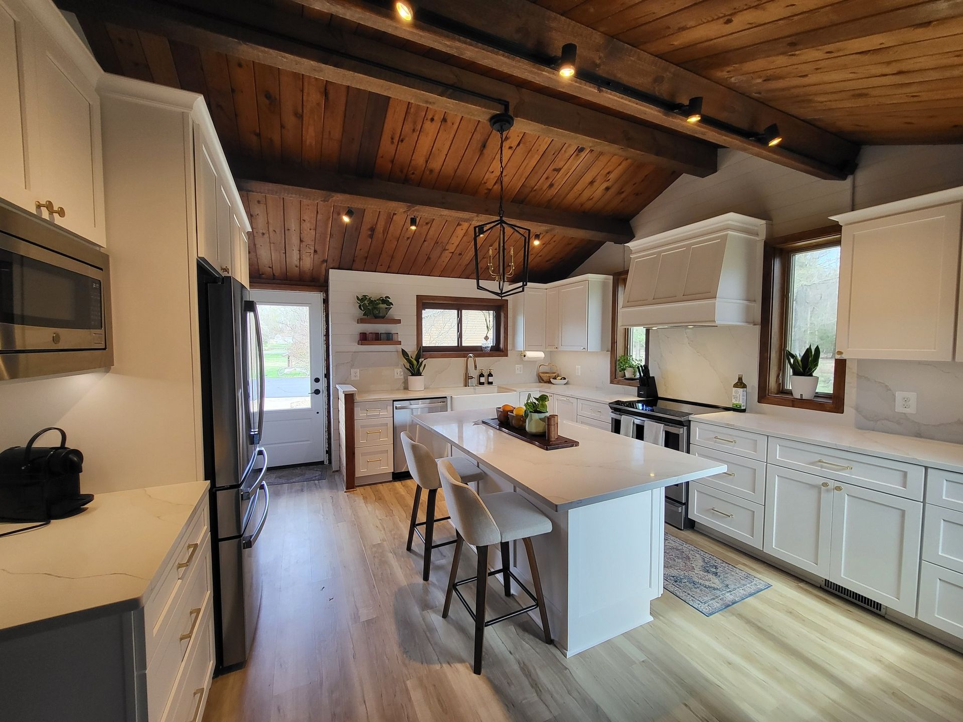 Bright kitchen with white cabinets, island, and appliances. Wooden ceiling with dark beams.