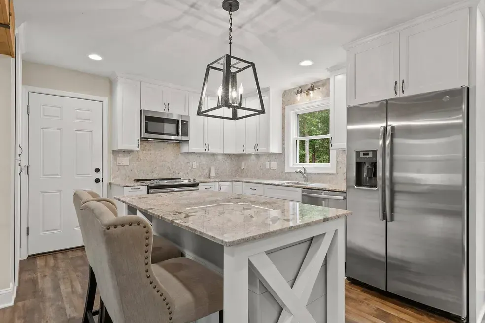 Modern white kitchen with island, stainless steel appliances, and dark wood floors.