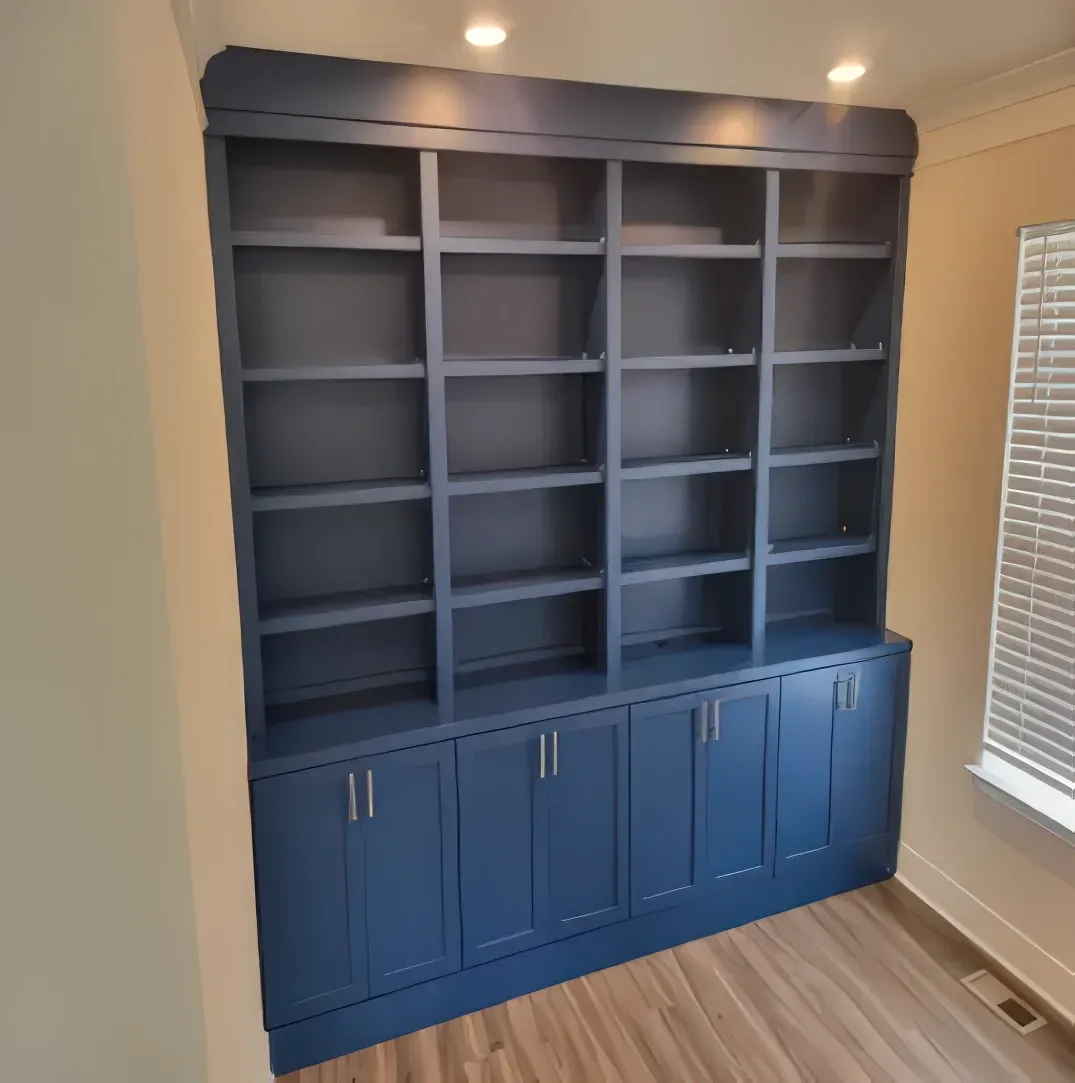 Built-in blue bookshelf with multiple shelves and cabinets in a room with a window and wood-look flooring.