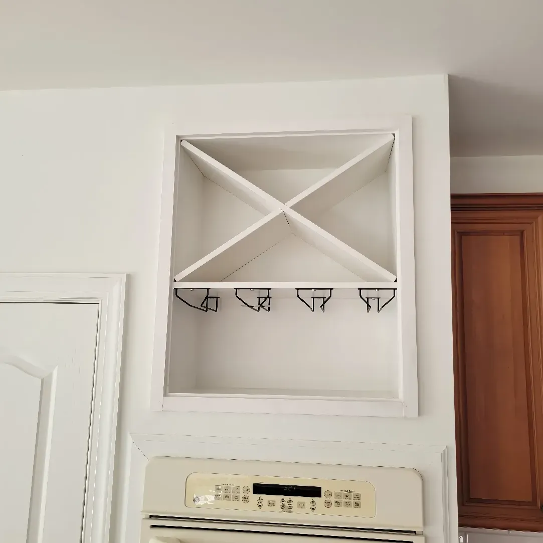 White wine rack built into the wall above an oven in a kitchen.
