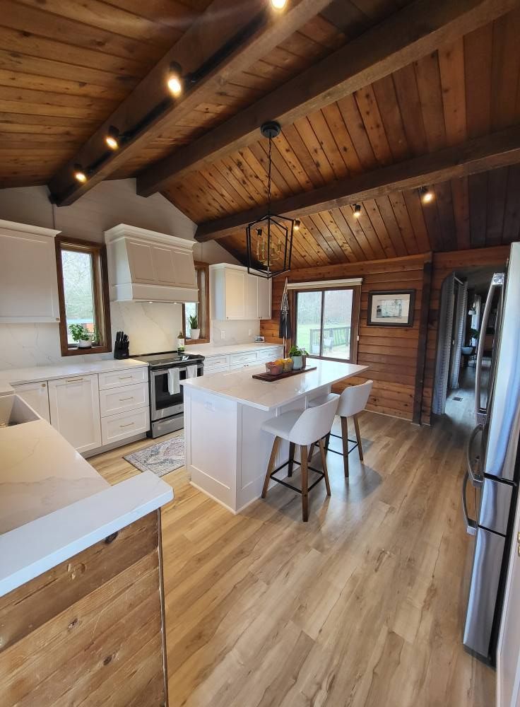 Kitchen with wood ceiling, white cabinets, island with stools, and sliding glass door.