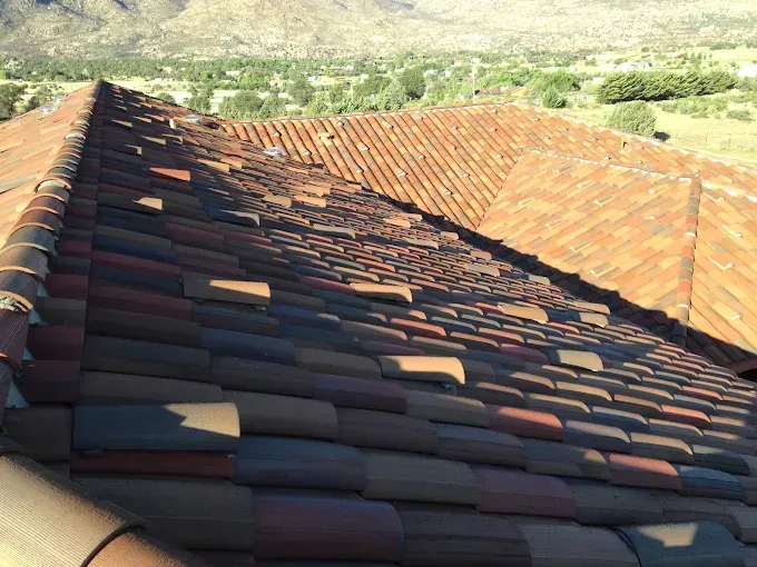 Clay tile roof on a building, angled view, brown and orange tiles, distant mountains and trees.