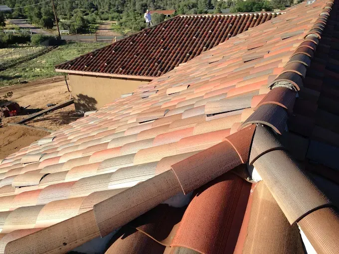Clay tile roof on a building, angled view, red and brown tones. A person stands on a nearby rooftop.