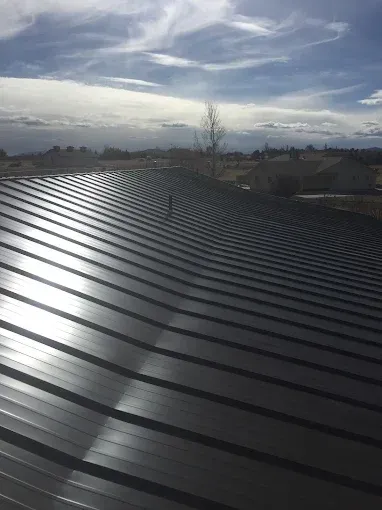 Dark metal roof reflecting sunlight, blue sky with clouds in the background.