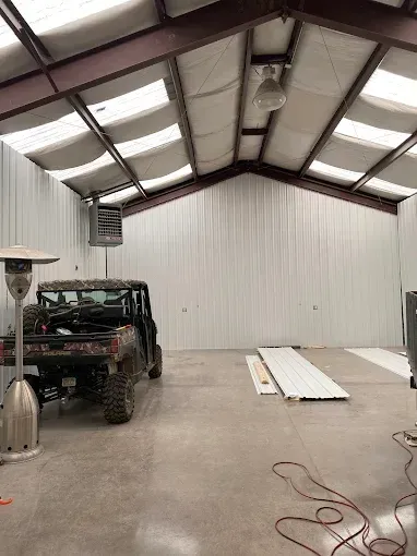 Interior of a large garage. A camo utility vehicle is parked inside. Metal beams and white walls.