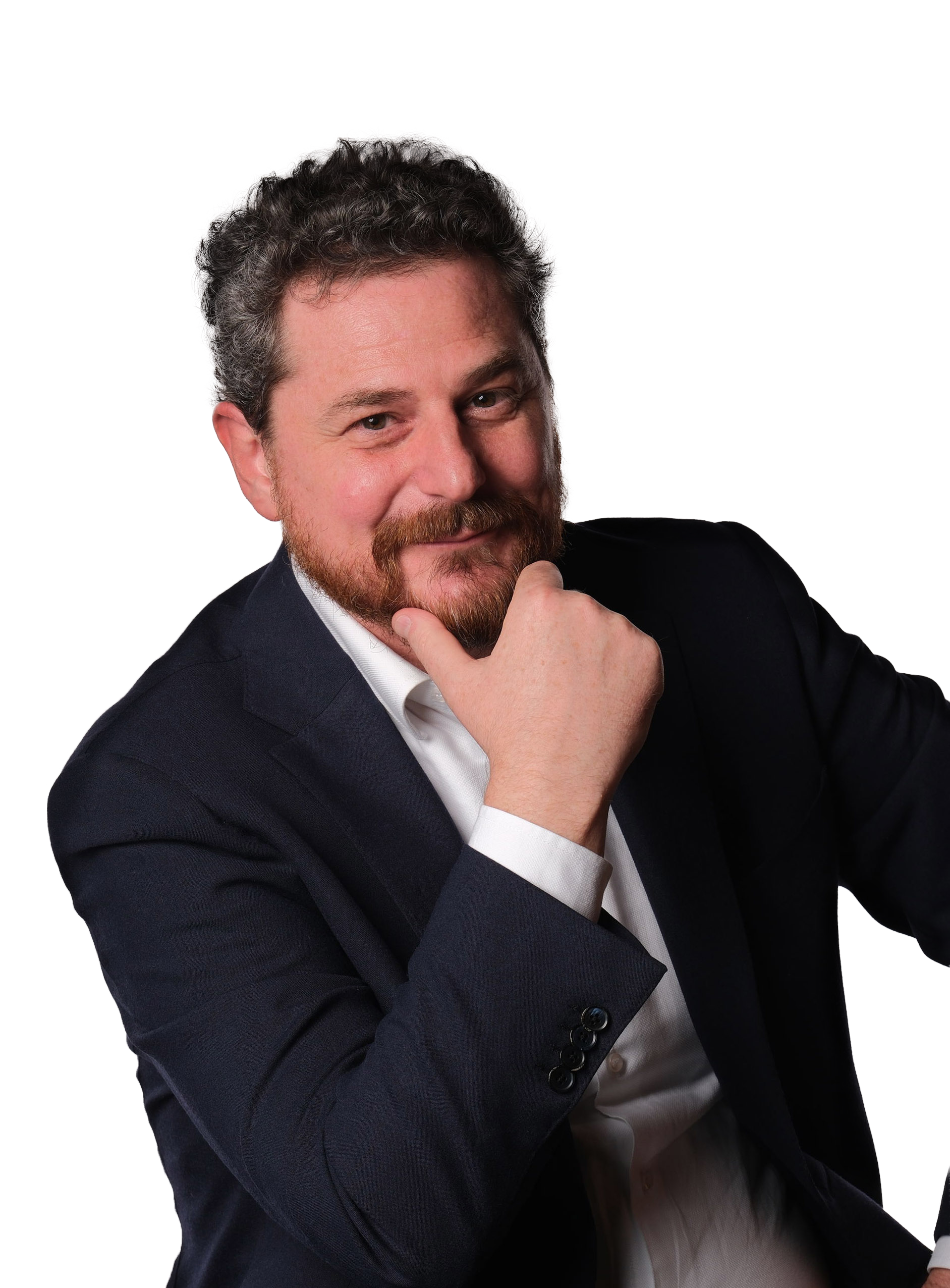 A person with short, dark curly hair and a beard wearing a dark blazer over a white shirt, resting their chin on a hand.