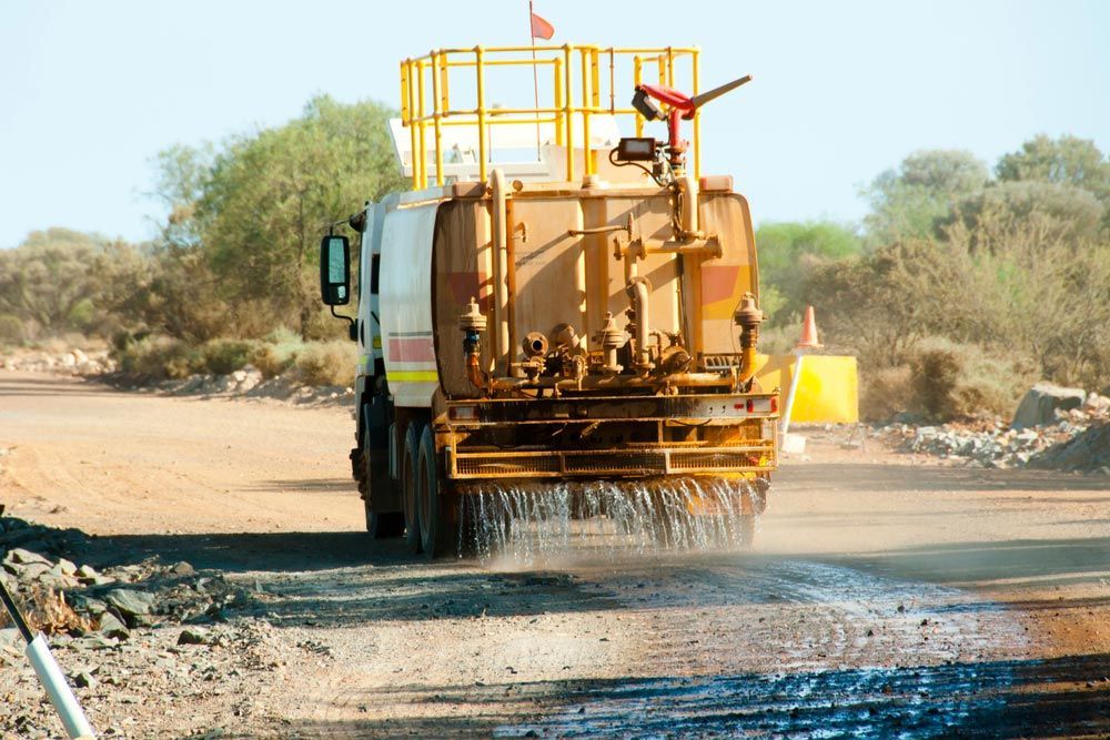 A Yellow Truck is Driving Down a Dirt Road — Nabiac Water Carriers in Wingham, NSW