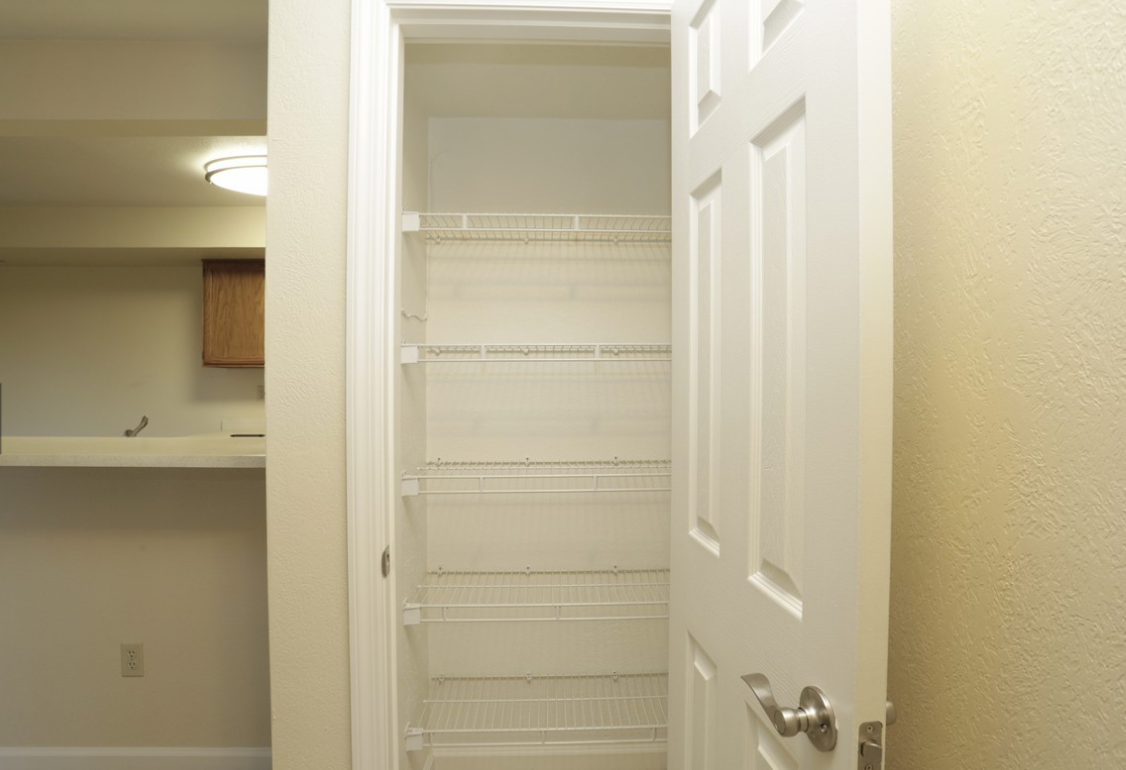 Open white pantry with wire shelves; adjacent to a kitchen area.