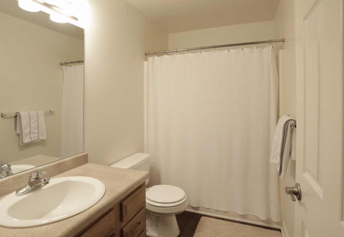 Bathroom with white shower curtain, toilet, vanity, and towel rack.