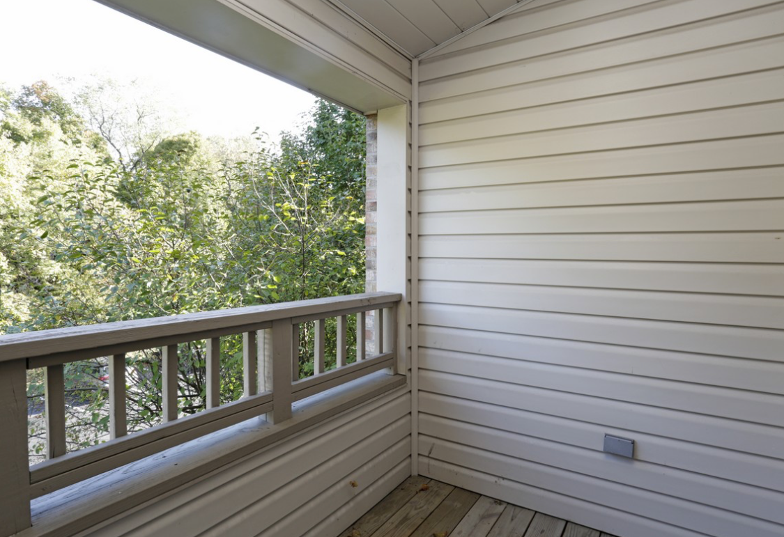 A wooden balcony overlooking trees, with white siding and a railing.