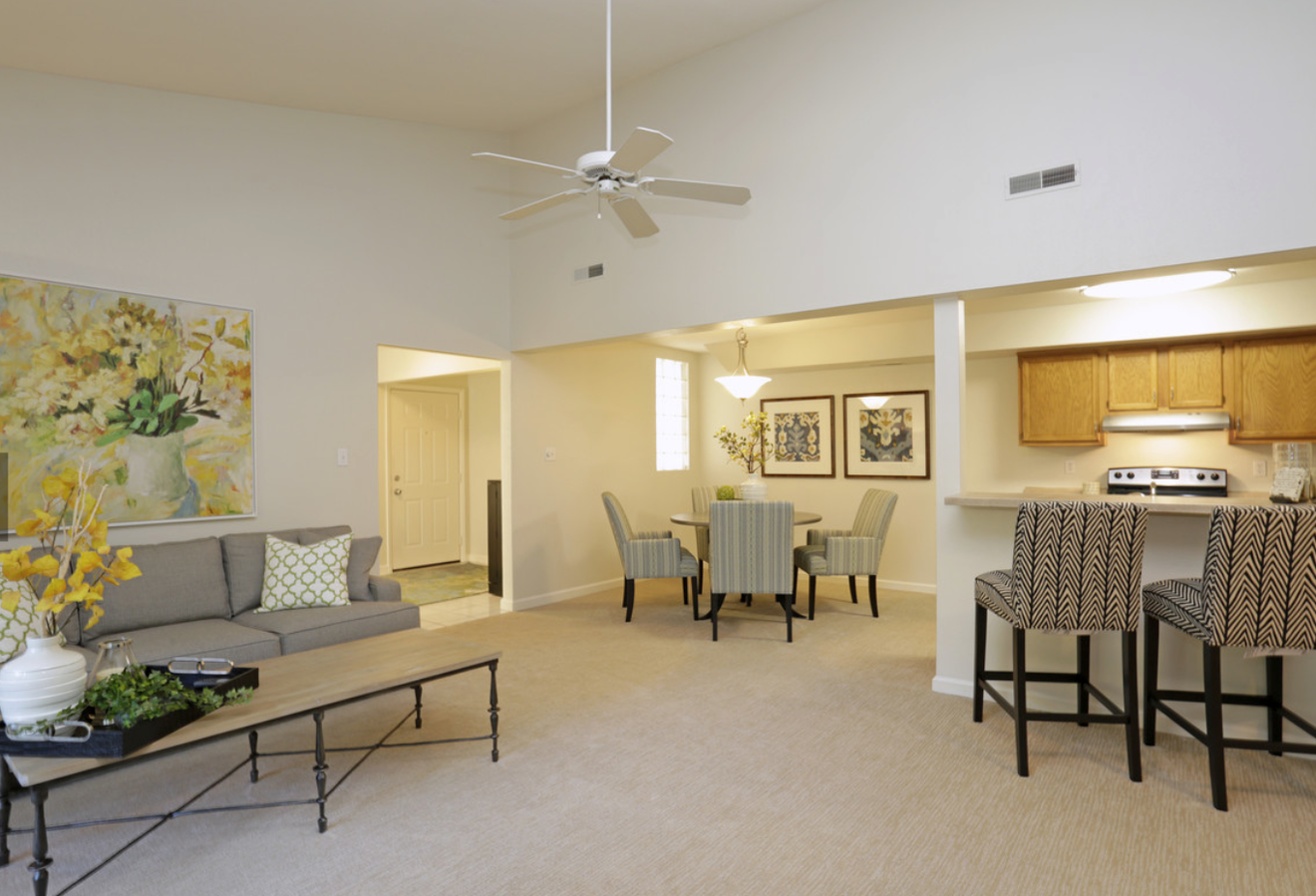 Spacious living room with a sofa, dining area, and kitchen. Beige walls, light carpet, and modern furniture.