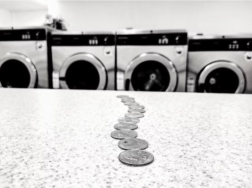 Coins lined up across a laundromat counter with washing machines in the background