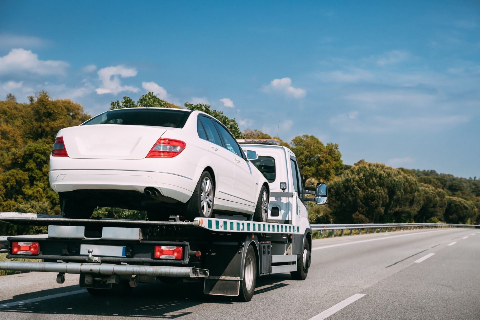 A White Car Is Being Towed By A Tow Truck On A Highway — Torquay & Anglesea Accident Towing Centre In Torquay, VIC