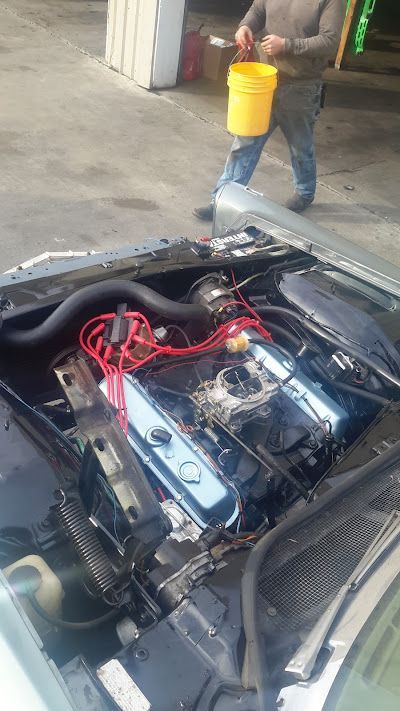 A man is cleaning the engine of a car with a yellow bucket.