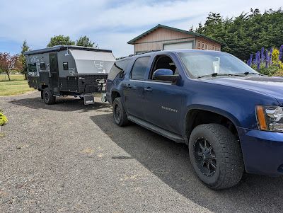 A blue suv is towing a trailer in a gravel lot.