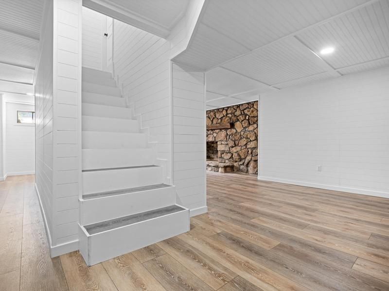 A basement with stairs leading up to the second floor and a fireplace.