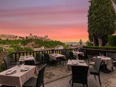 A restaurant with tables and chairs with a view of a city at sunset.