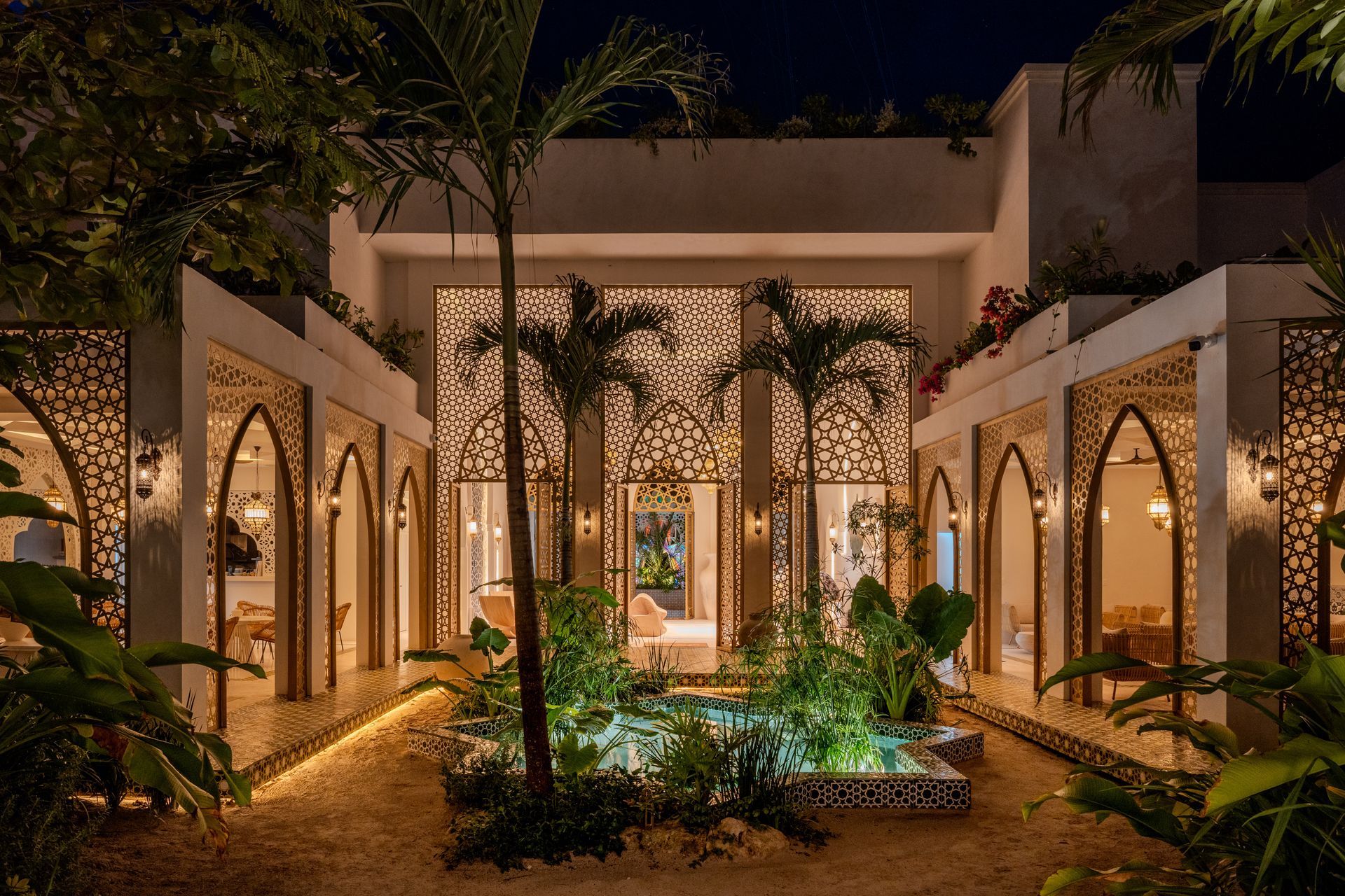 Exterior nighttime view of an elegant, open-air courtyard with intricate latticework, lush greenery, and soft lighting.