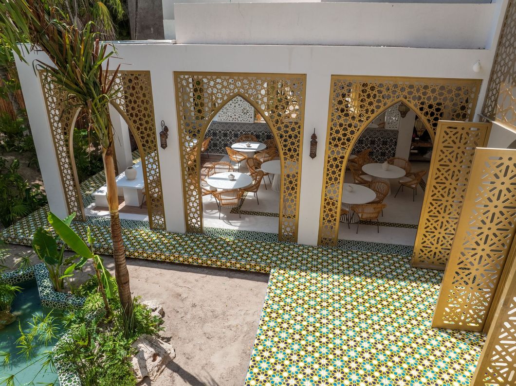 Outdoor restaurant with white and gold decorative arches, tables, and green/gold tiled floor.
