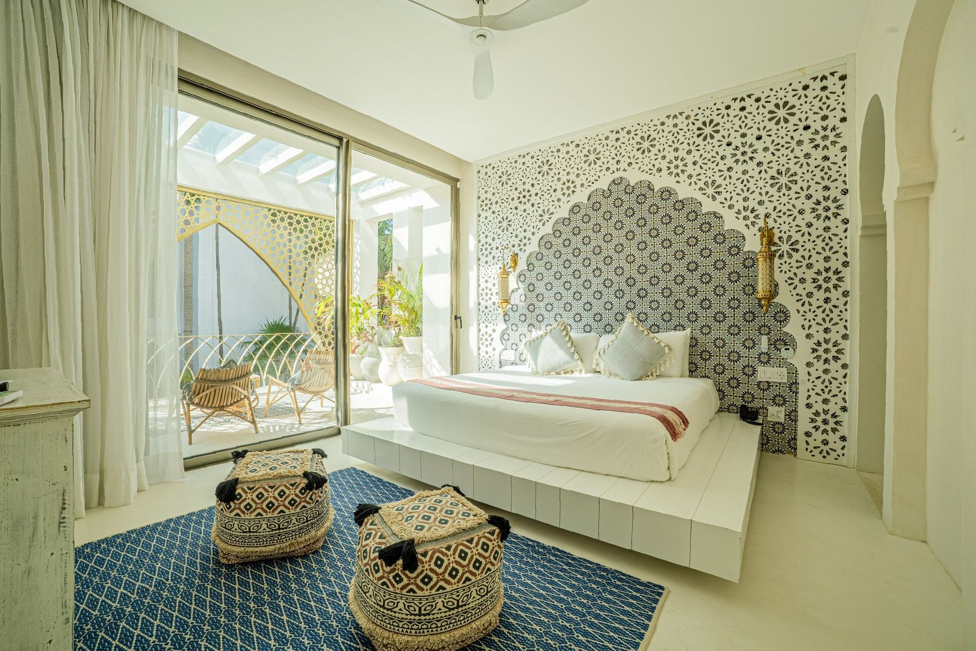 Living room with teal sofa, ornate white arch window, patterned rug, and doorway to bedroom.