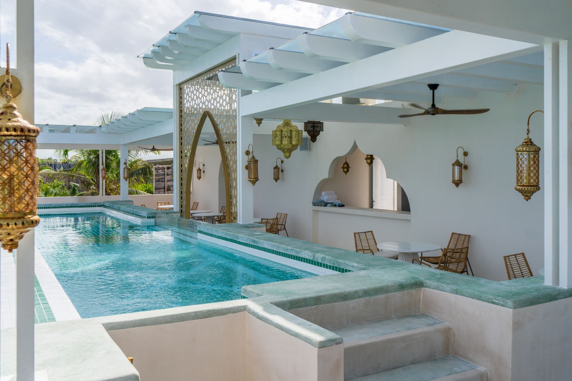 Piscina con azulejos turquesas, pérgola blanca y faroles de estilo marroquí.