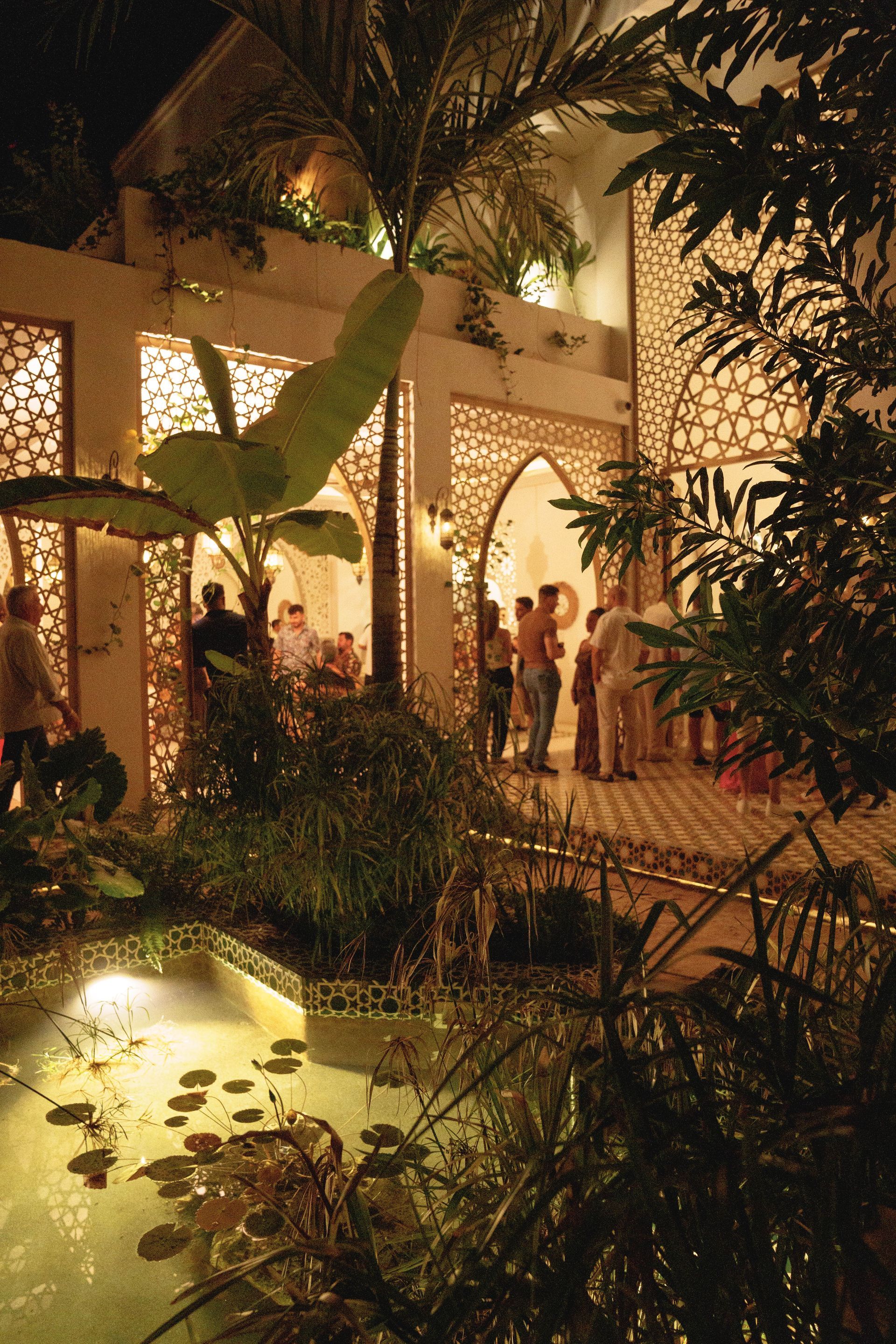 A building with patterned walls and arches, a fountain, and palm trees against a blue sky.