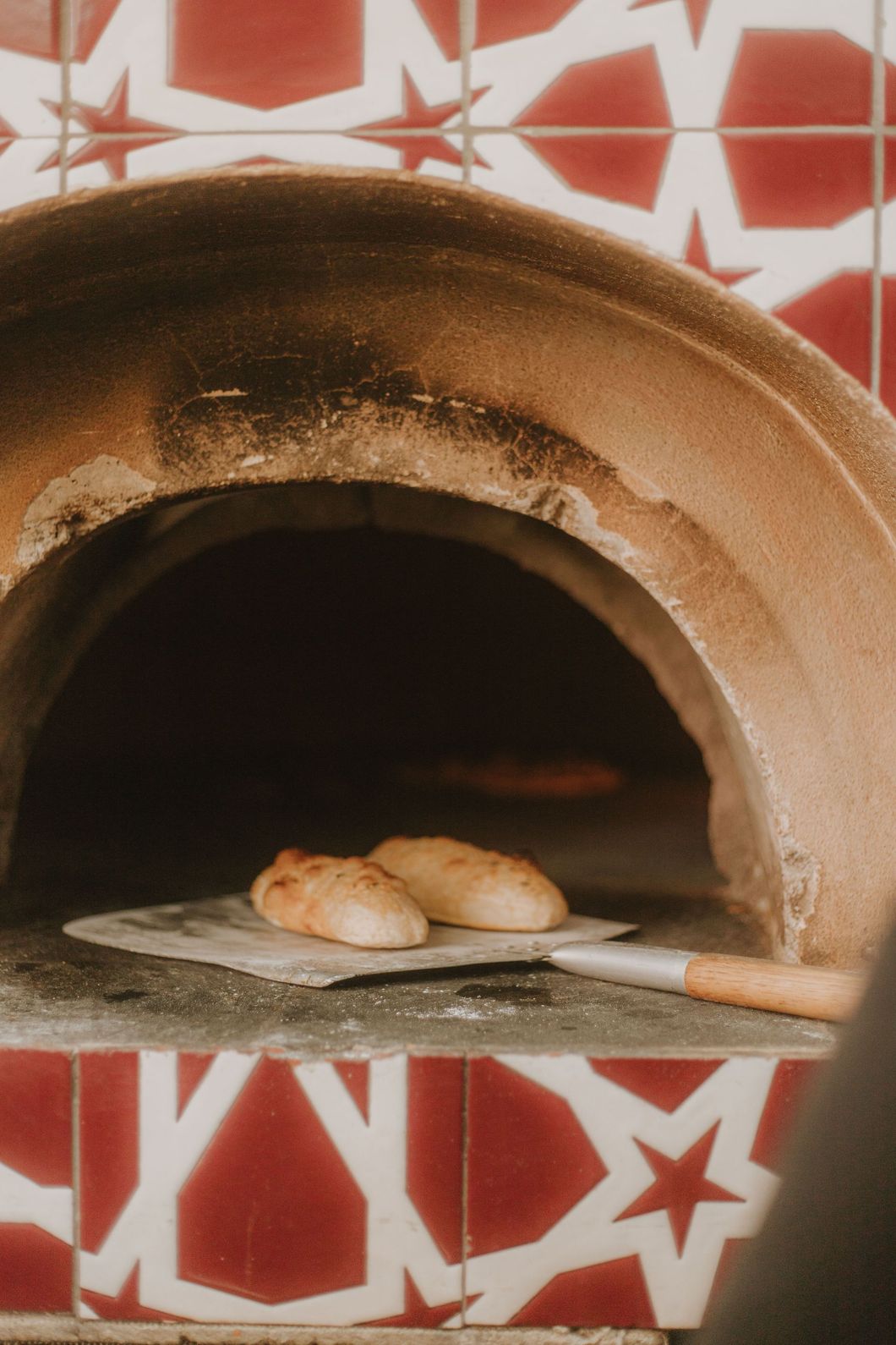 Two loaves of bread on a peel inside a brick oven. Red and white star tile pattern.