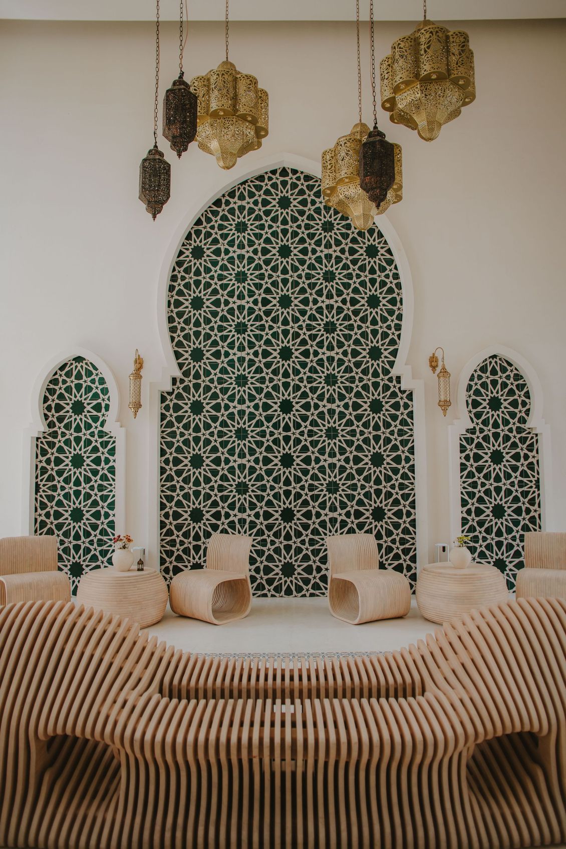Interior with ornate green tilework backdrop, wooden seating, and hanging gold lanterns.