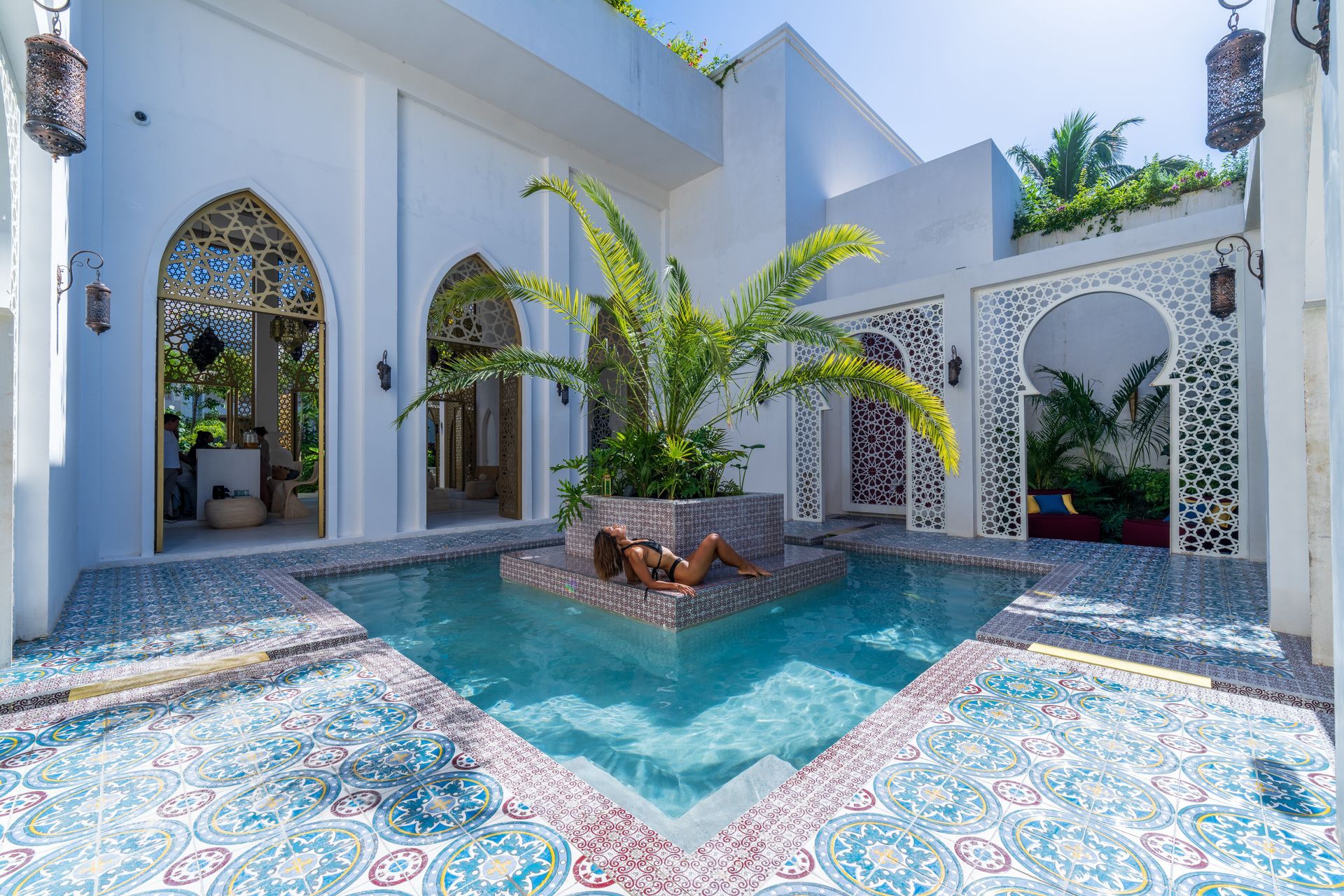 Courtyard with pool, ornate white walls, tiled floor, person sunbathing on central island.