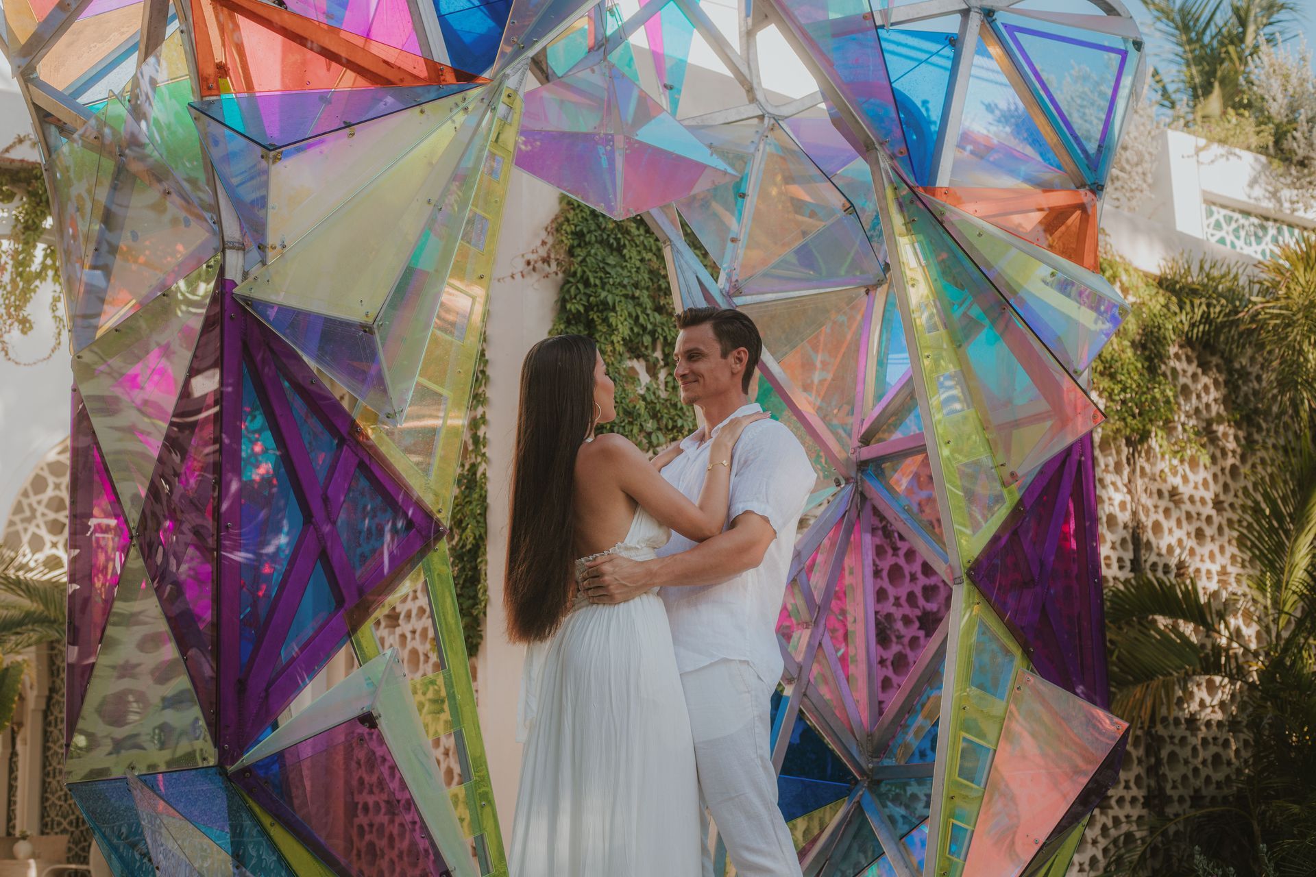 Couple embracing in front of a colorful geometric art installation, outdoors.
