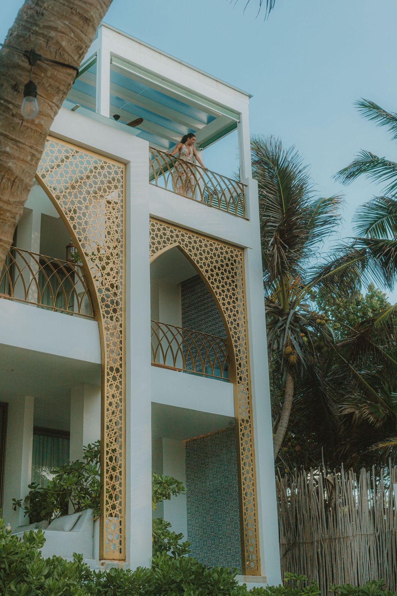 White building with gold arabesque design, person on balcony, palm trees.