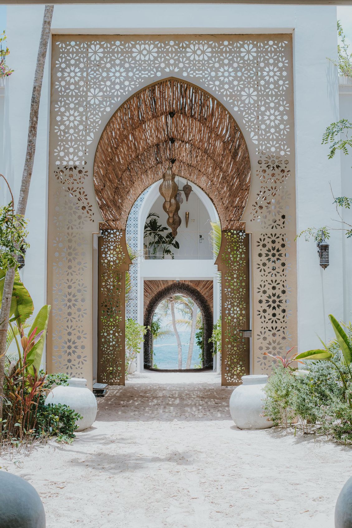 Ornate archway with intricate patterns, leading to a series of doorways and a view of the sea.