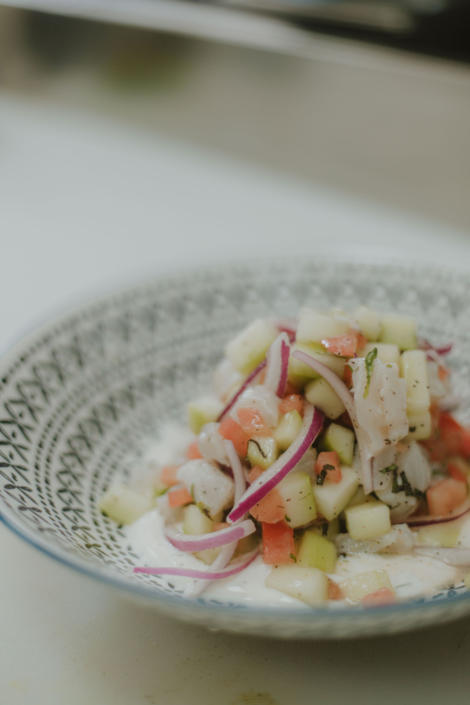 Ceviche in a patterned bowl, featuring diced vegetables and fish.