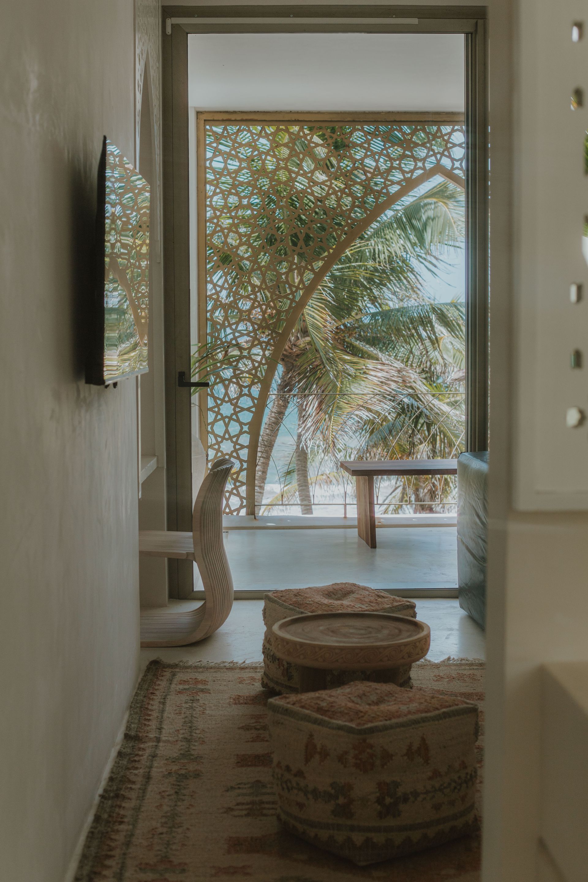 Interior view with decorative screen, opening to outdoor view of palm trees, seating, and rug.