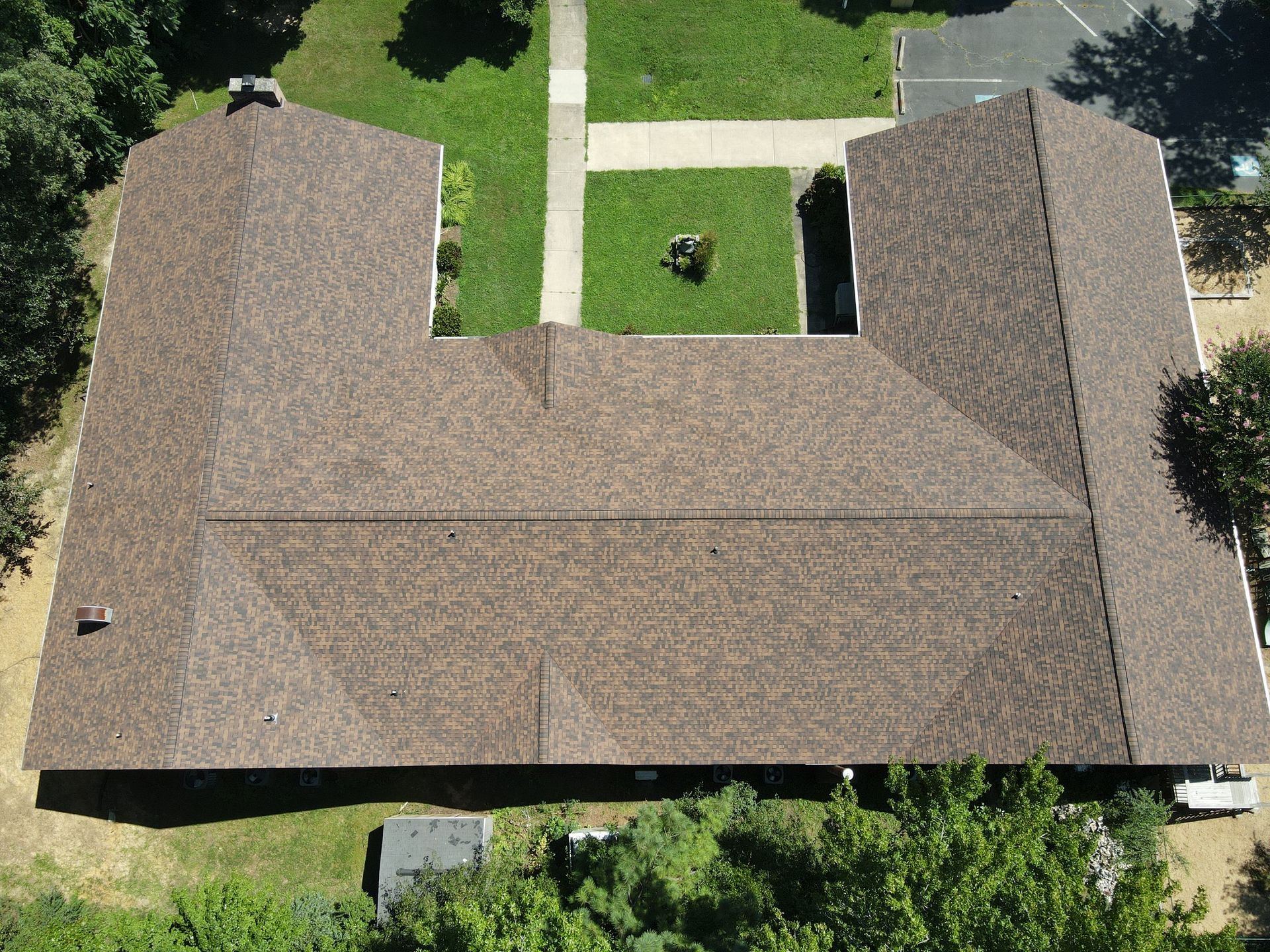 An aerial view of a large house with a brown roof surrounded by trees and grass.