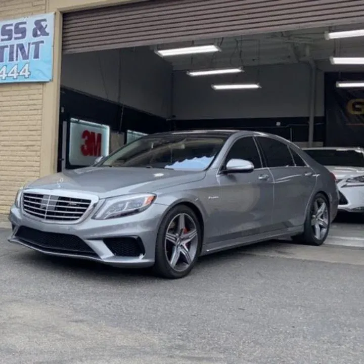 Silver Mercedes-Benz sedan parked in front of a garage with a tint shop sign.