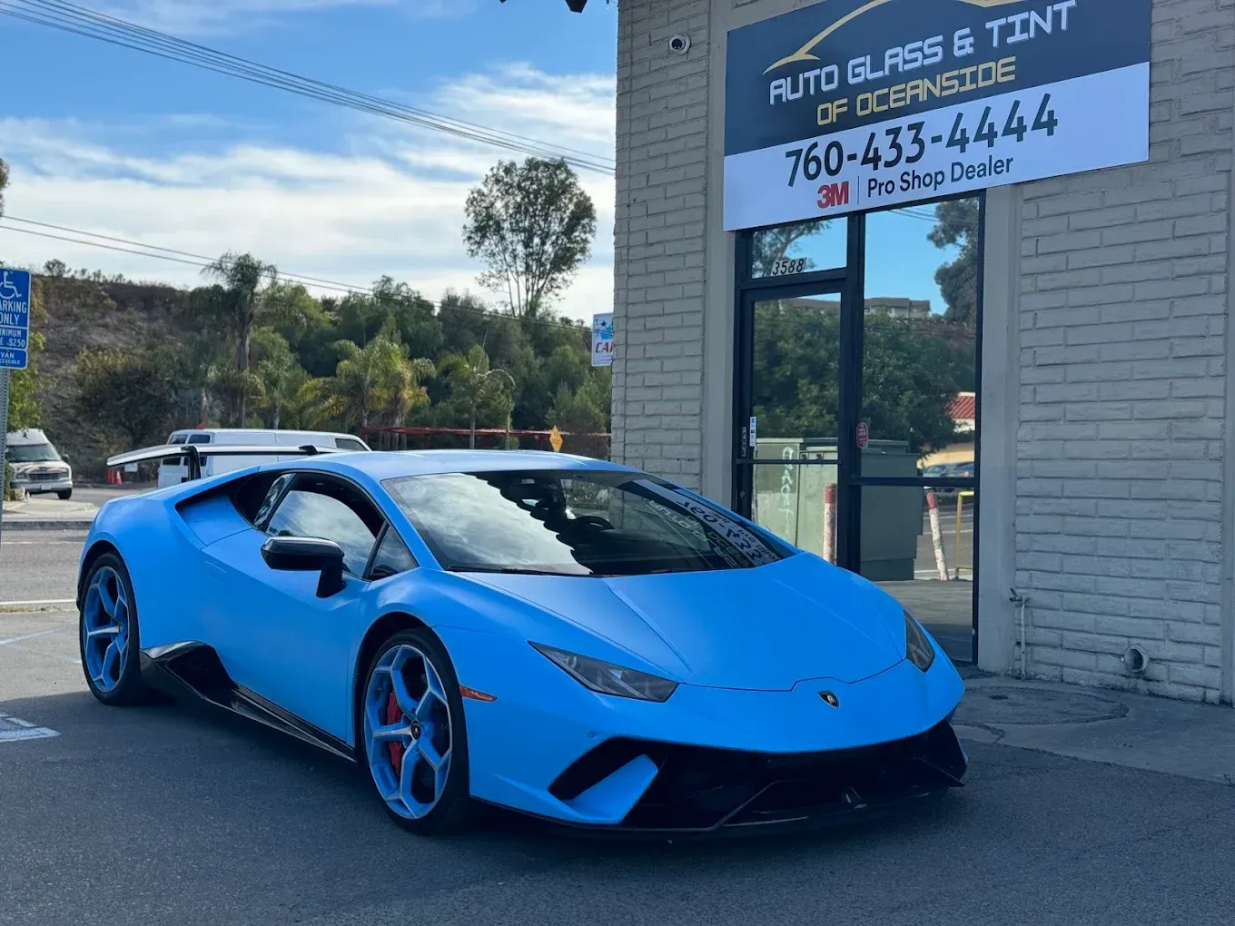 Blue Lamborghini sports car parked outside an auto glass and tint shop.
