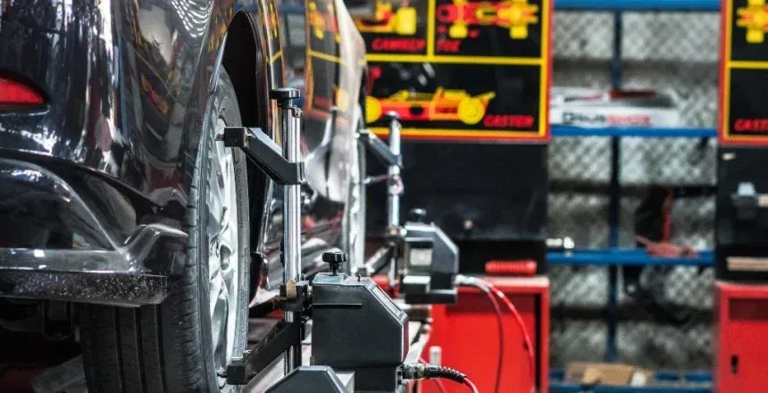 Car on a lift at a mechanic shop being aligned, with sensors attached to the wheels, red and black color scheme.