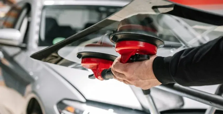 Person using suction cups to install a car windshield on a silver vehicle.