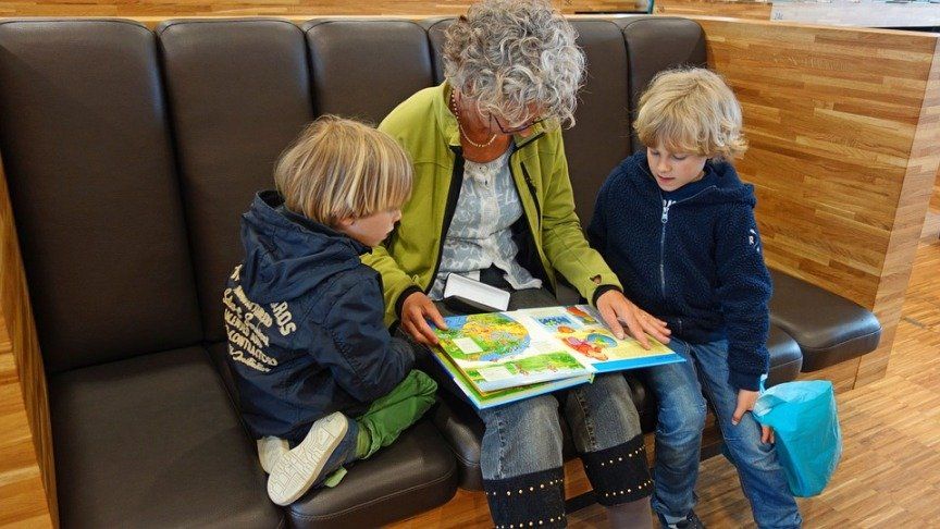 grandma reading book to her grandchildren in a waiting area
