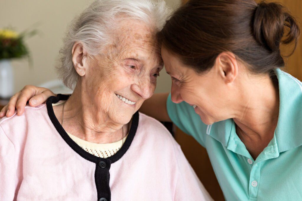 Caregiver and elderly woman touching foreheads while smiling