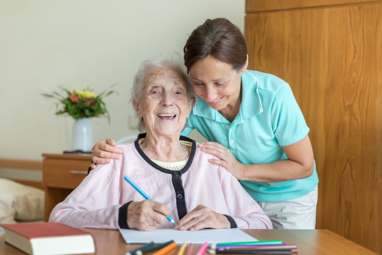 A smiling dementia patient with her caregiver, coloring