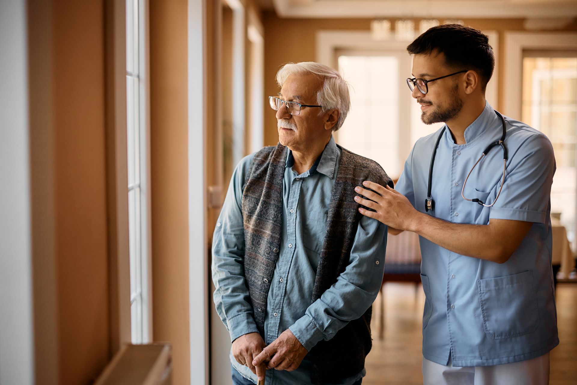 male caregiver with senior man looking out a window