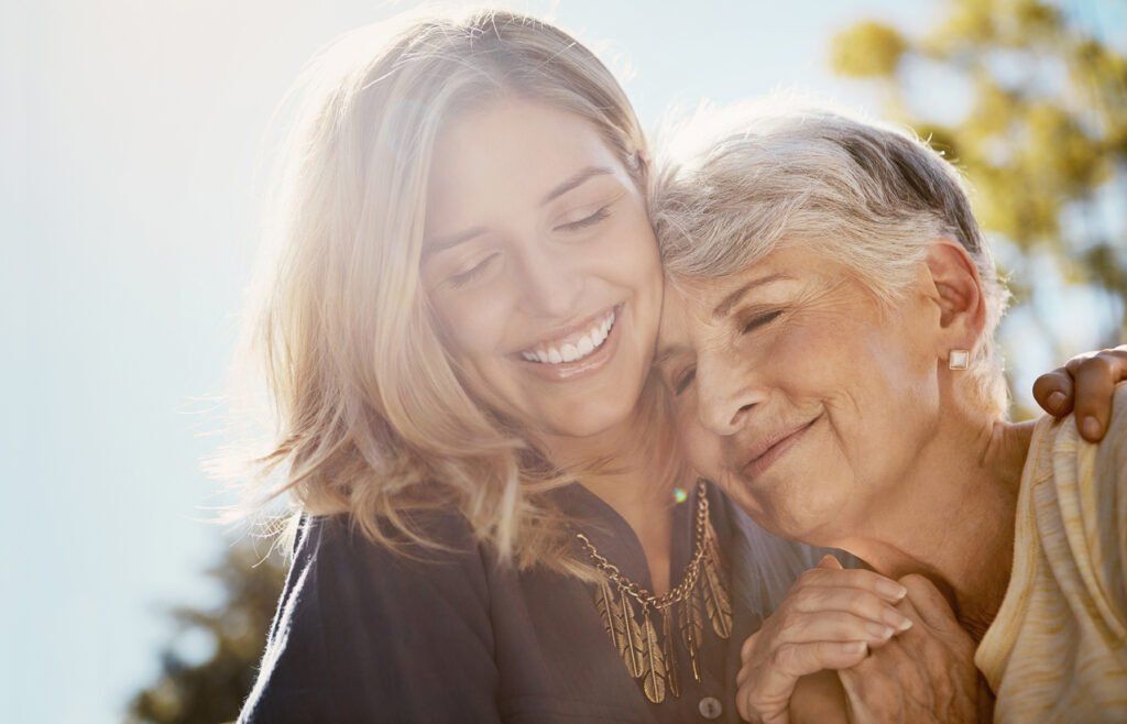 adult daughter and elderly mother embracing and smiling