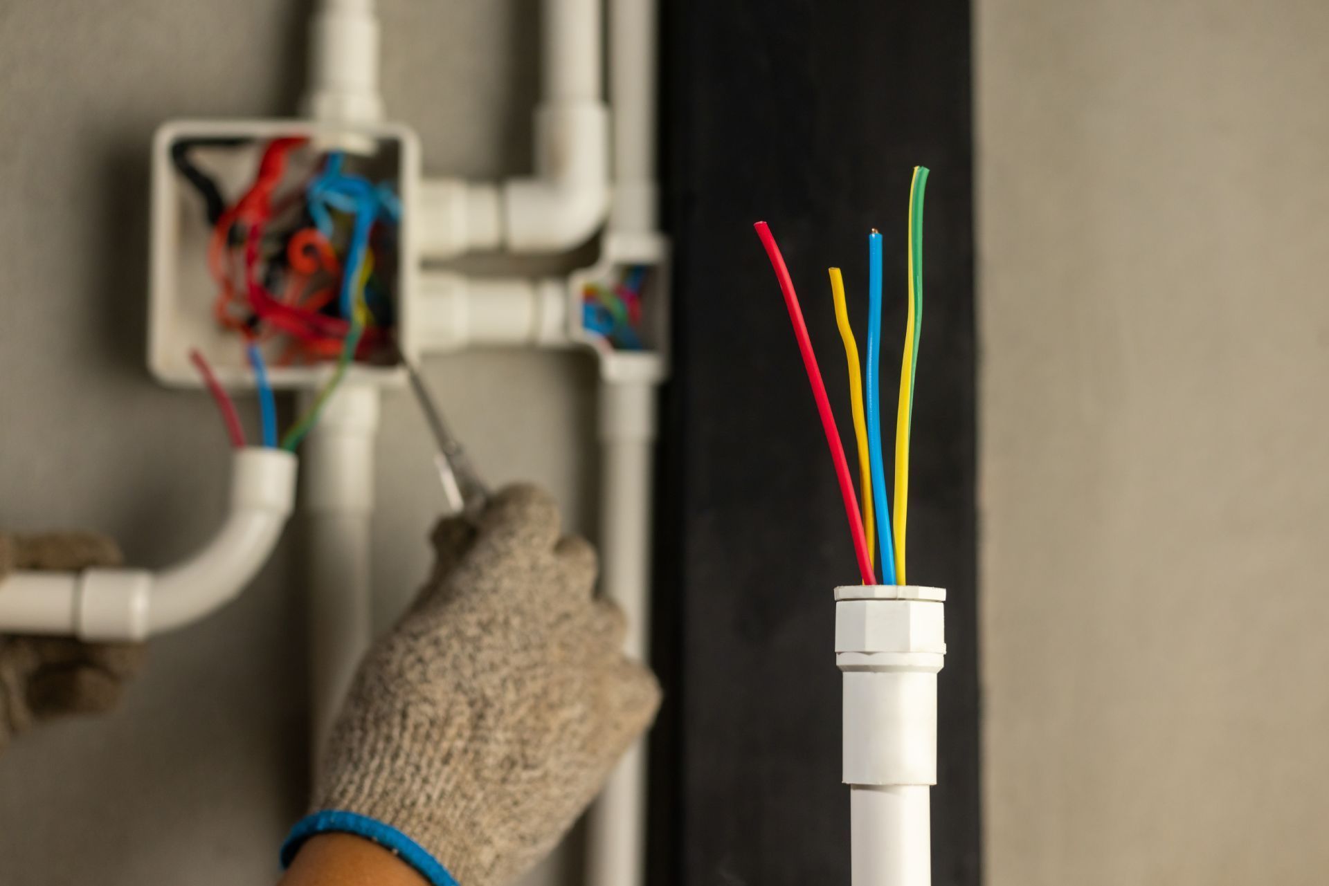 Electrician working on wires inside electrical conduit and junction boxes.