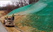 Worker spraying green material onto a hillside from a truck to prevent erosion.