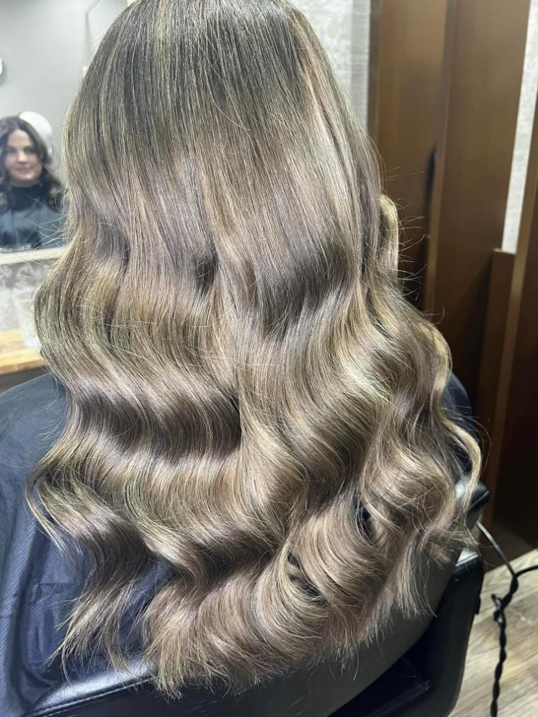 A Woman with Long Blonde Hair Is Standing in Front of A Wall of Flowers — Losh Hair Lounge In Toowoomba City, QLD