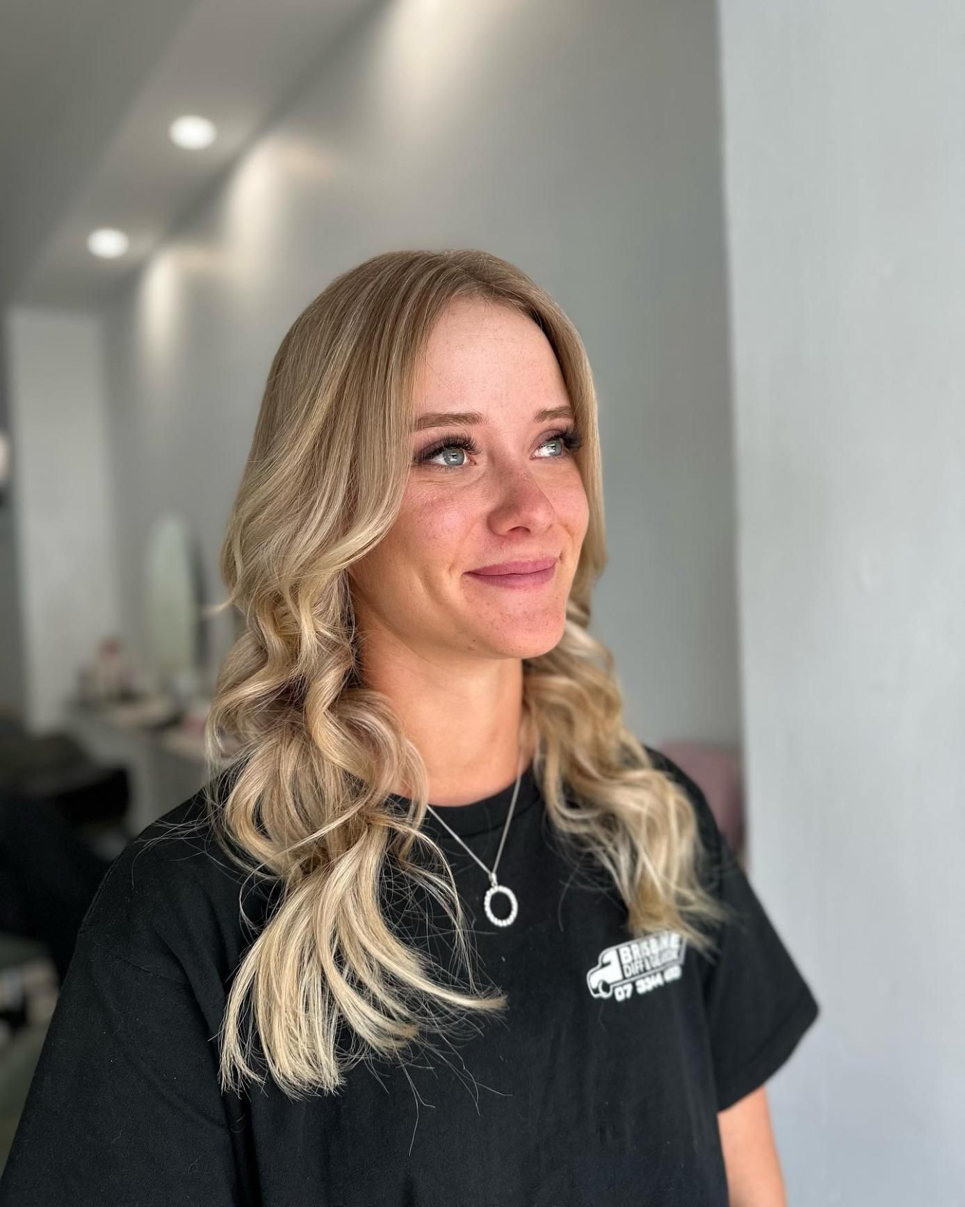 A Woman with Blonde Hair Is Wearing a Black Shirt and A Necklace — Losh Hair Lounge In Toowoomba City, QLD