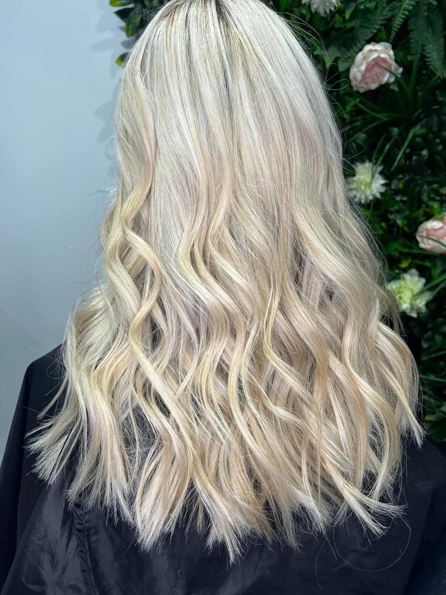 A Woman with Long Blonde Hair Is Standing in Front of A Wall of Flowers — Losh Hair Lounge In Toowoomba City, QLD